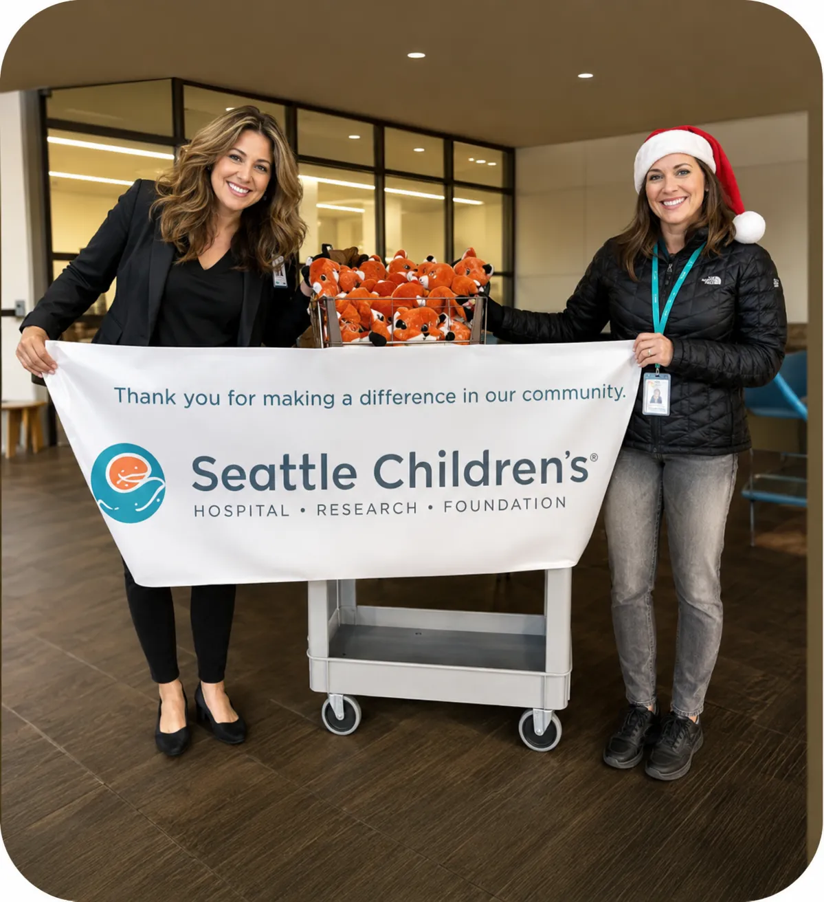Two event staff holding a Seattle Children's Hospital thank-you banner beside a cart of donated handmade plush foxes from a Noah's Ark Animal Workshop community event