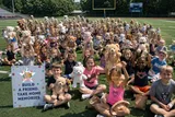 Rows of children at a large-group workshop on a field, working together on their stuffed animals