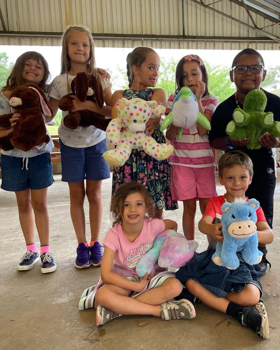 A group of kids at a pavilion event each holding the stuffed animal they made